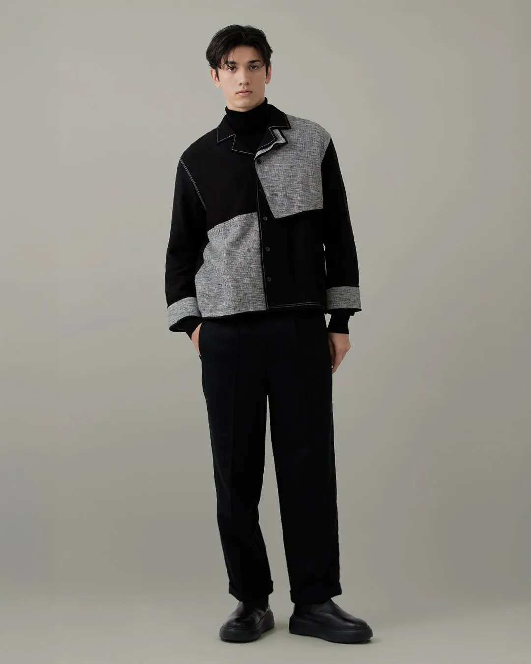 男性がパッチワークジャケット、黒パンツ、ブーツ