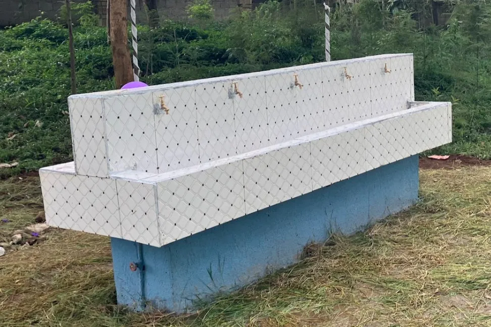 屋外に設置された水飲み場。白いタイル張りの壁に複数の蛇口が並び、青い台座の上に設置されている。