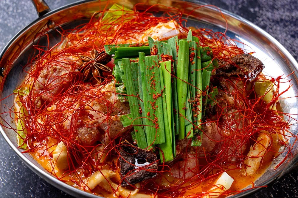 鍋料理の写真。赤い糸唐辛子とネギがトッピングされた料理が、銀色の鍋に入っている。