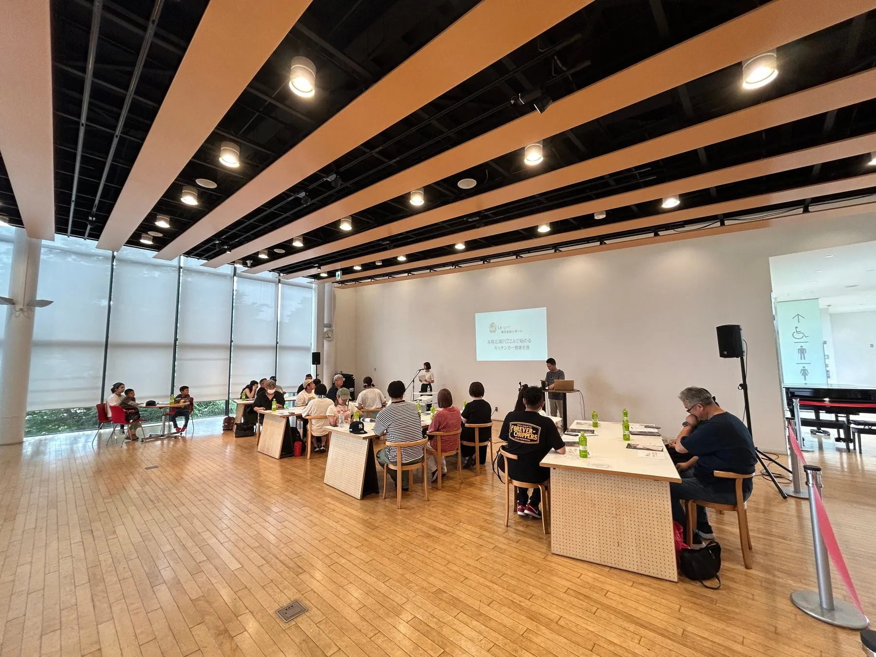 会議室で行われているセミナーの様子。プレゼンテーションが行われ、参加者がテーブルに着席している。