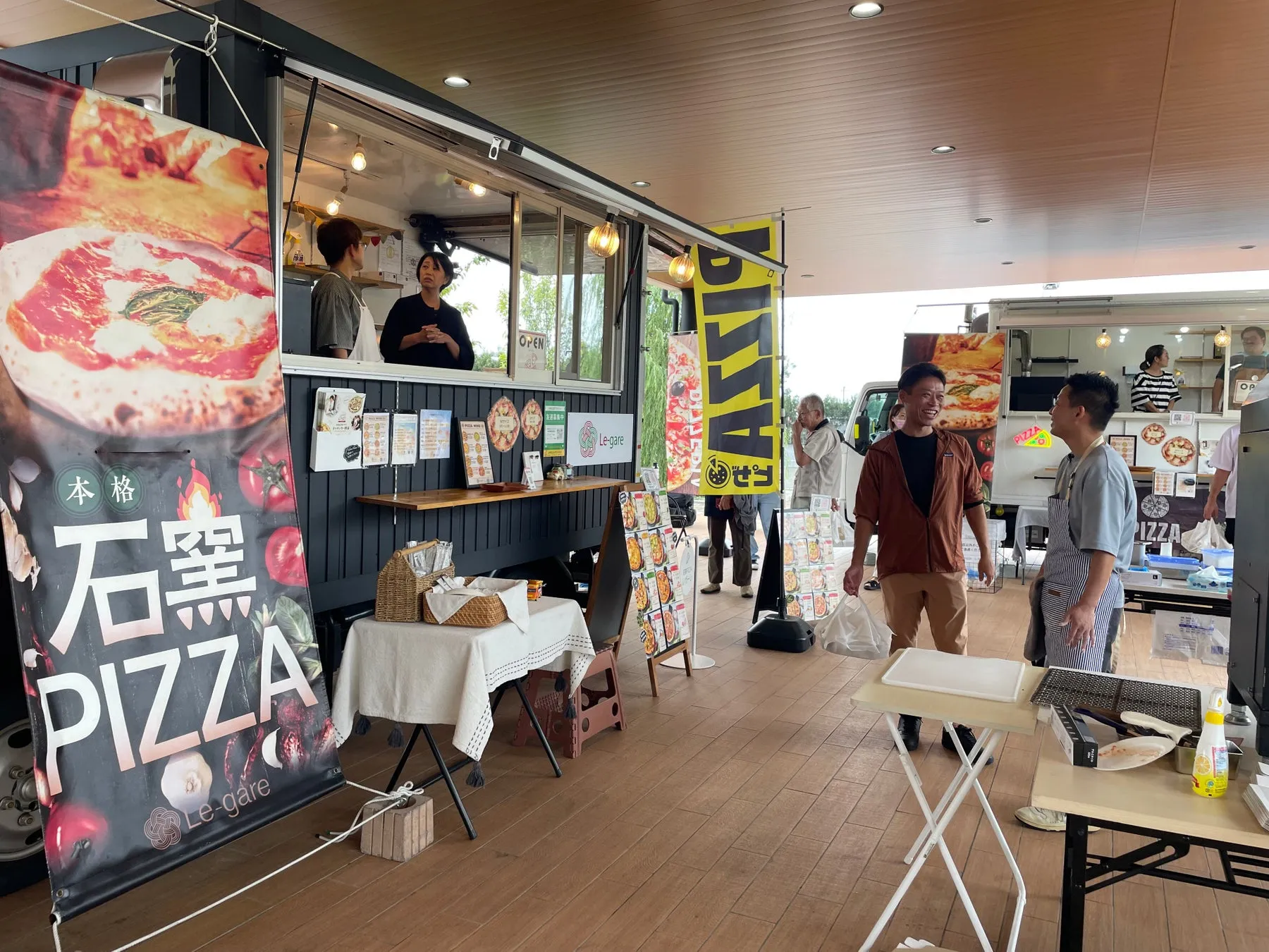ピザのキッチンカーが出店している様子。お店の人や、お客さんが写っています。