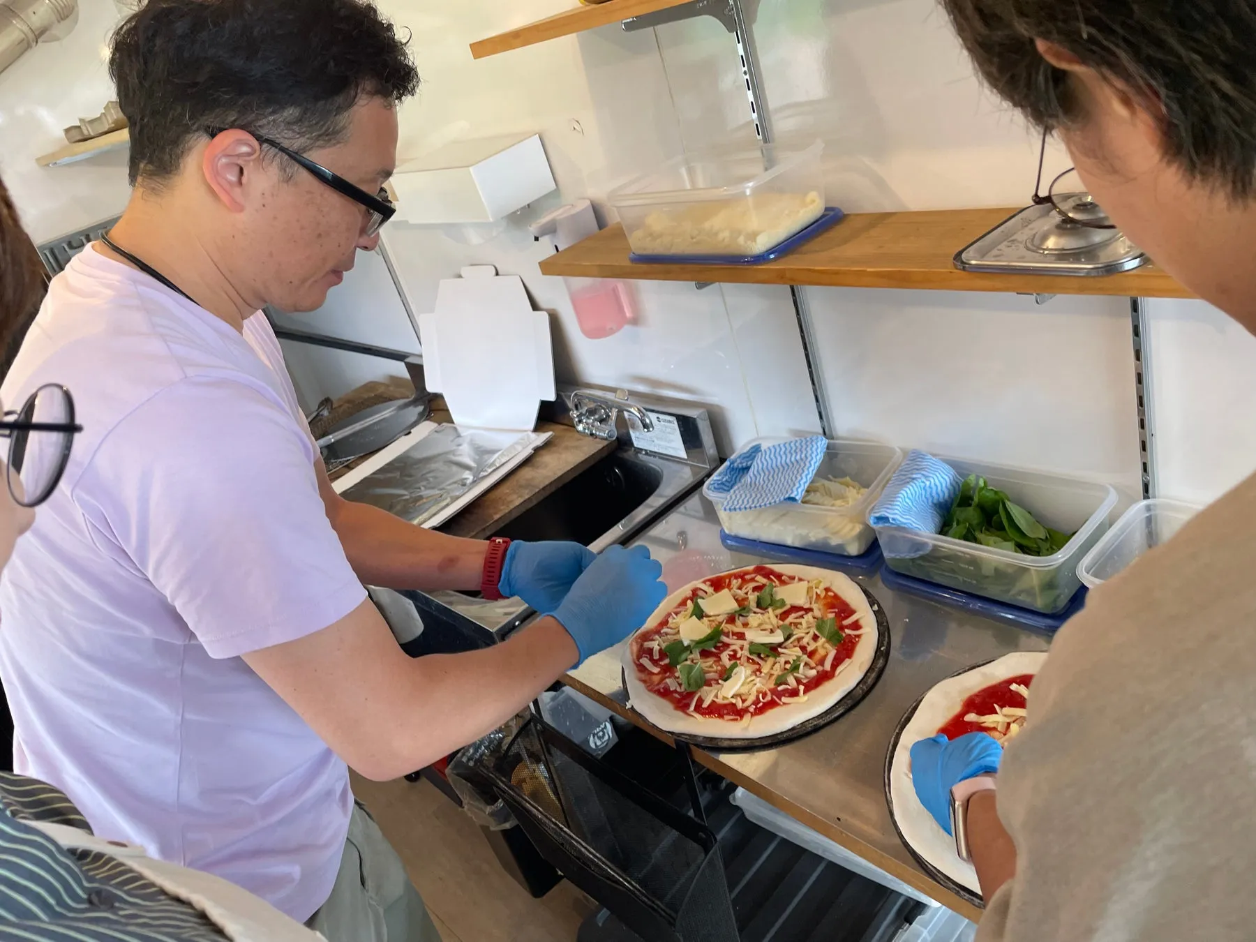 男性が2人でピザを作っている様子。ピザ生地に具材を乗せているところ。