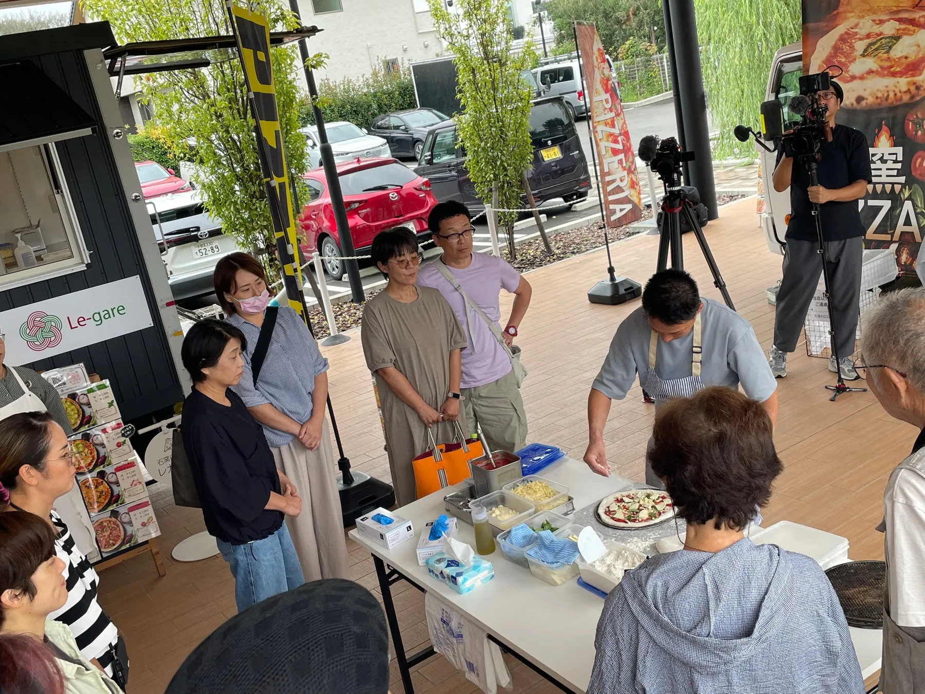 ピザ作りのデモンストレーションが行われている様子。周りには見物客が集まり、カメラも回っている。