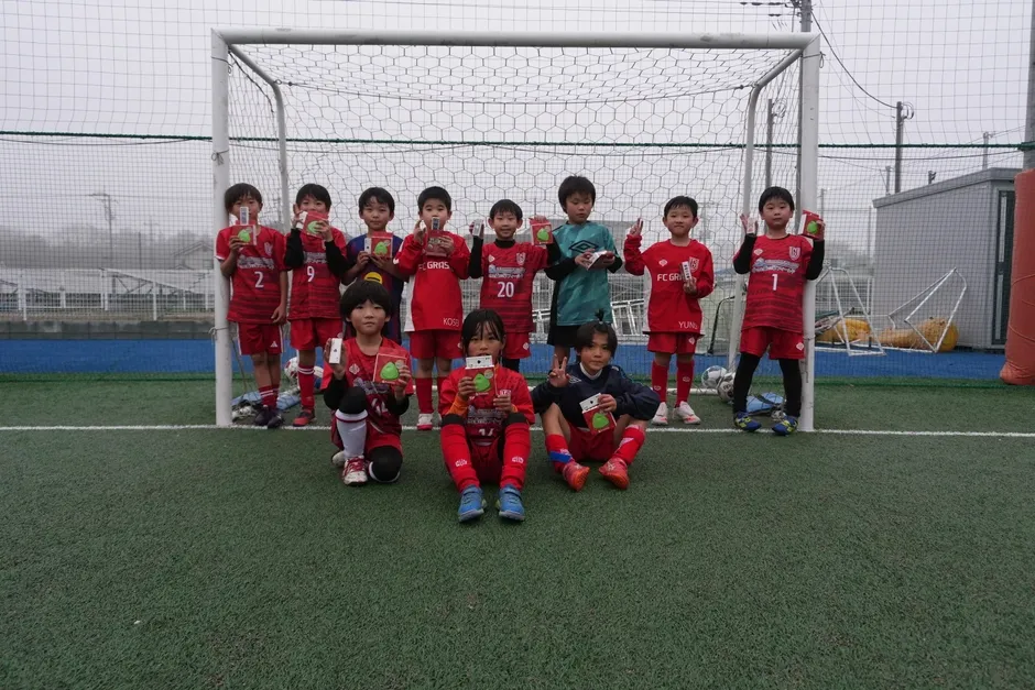 サッカーチームの少年たちが、プレゼントを持ってみんなで記念写真に写っている様子です。
