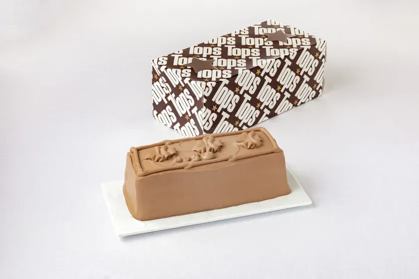 チョコレートケーキとそれを包む箱の写真。箱には「Tops」のロゴが繰り返しプリントされており、ケーキは長方形で、表面に装飾が施されている。
