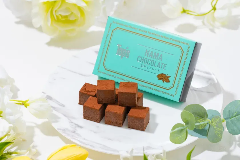 生チョコレートの箱とチョコレートのキューブが、白い皿の上に置かれています。周りには花が飾られています。