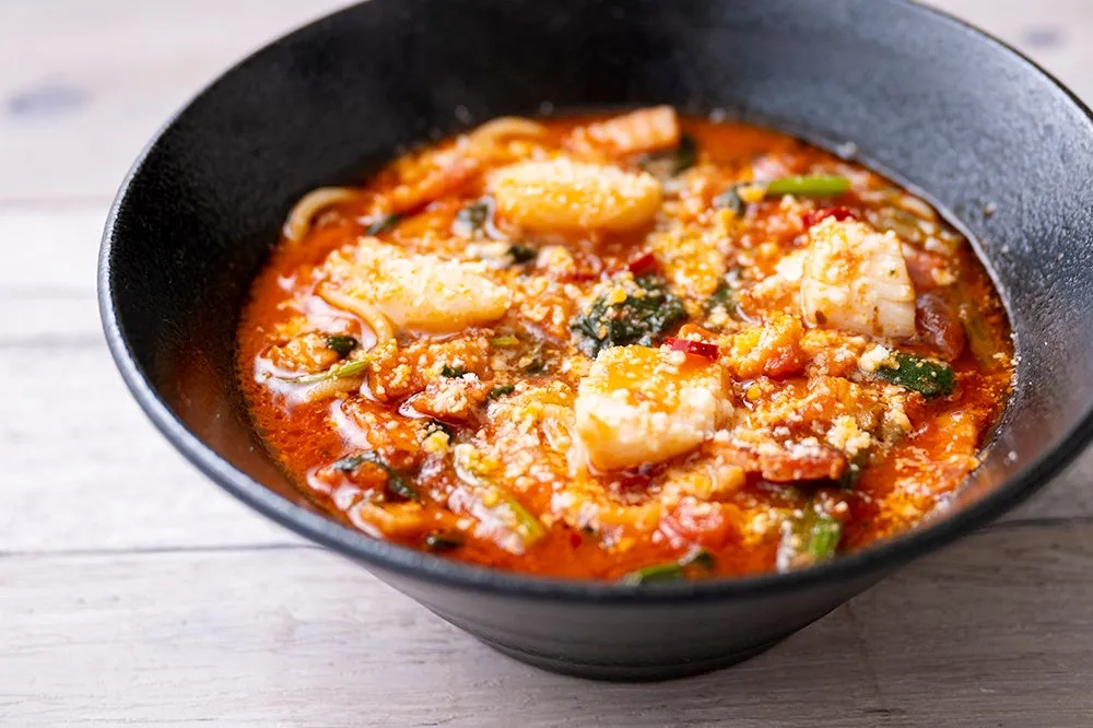 黒い器に入った、エビと野菜のトマトソースパスタの写真です。パスタの上には粉チーズがかけられています。