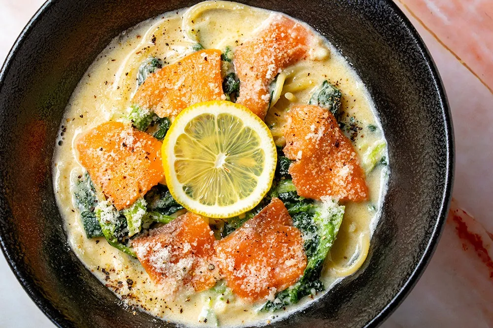 サーモンとレモンのパスタのクローズアップ写真。黒いボウルに入った料理で、レモンスライスが真ん中に配置されています。