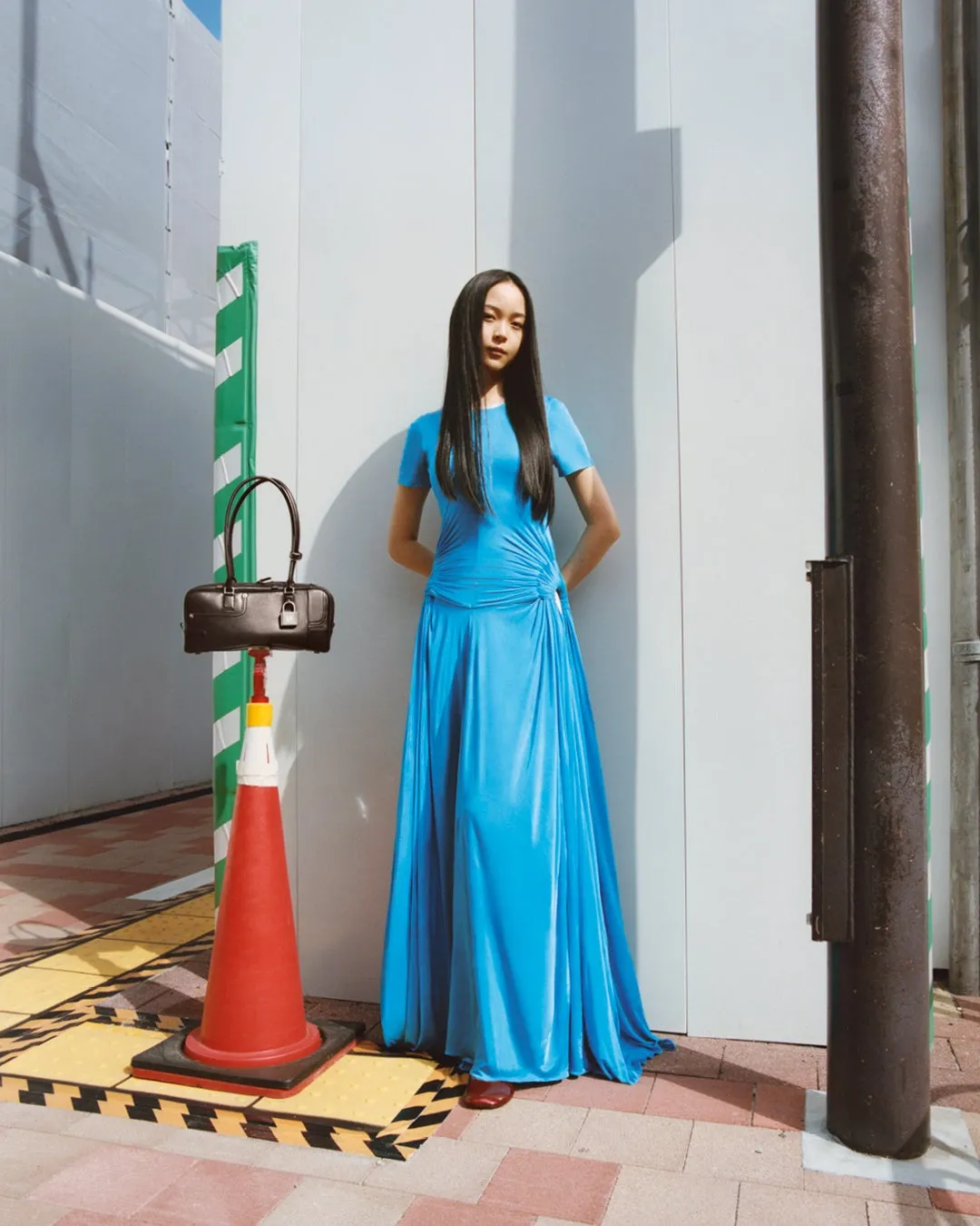 青いドレスを着た女性が、路上に置かれたバッグとコーンの前で立っている写真。