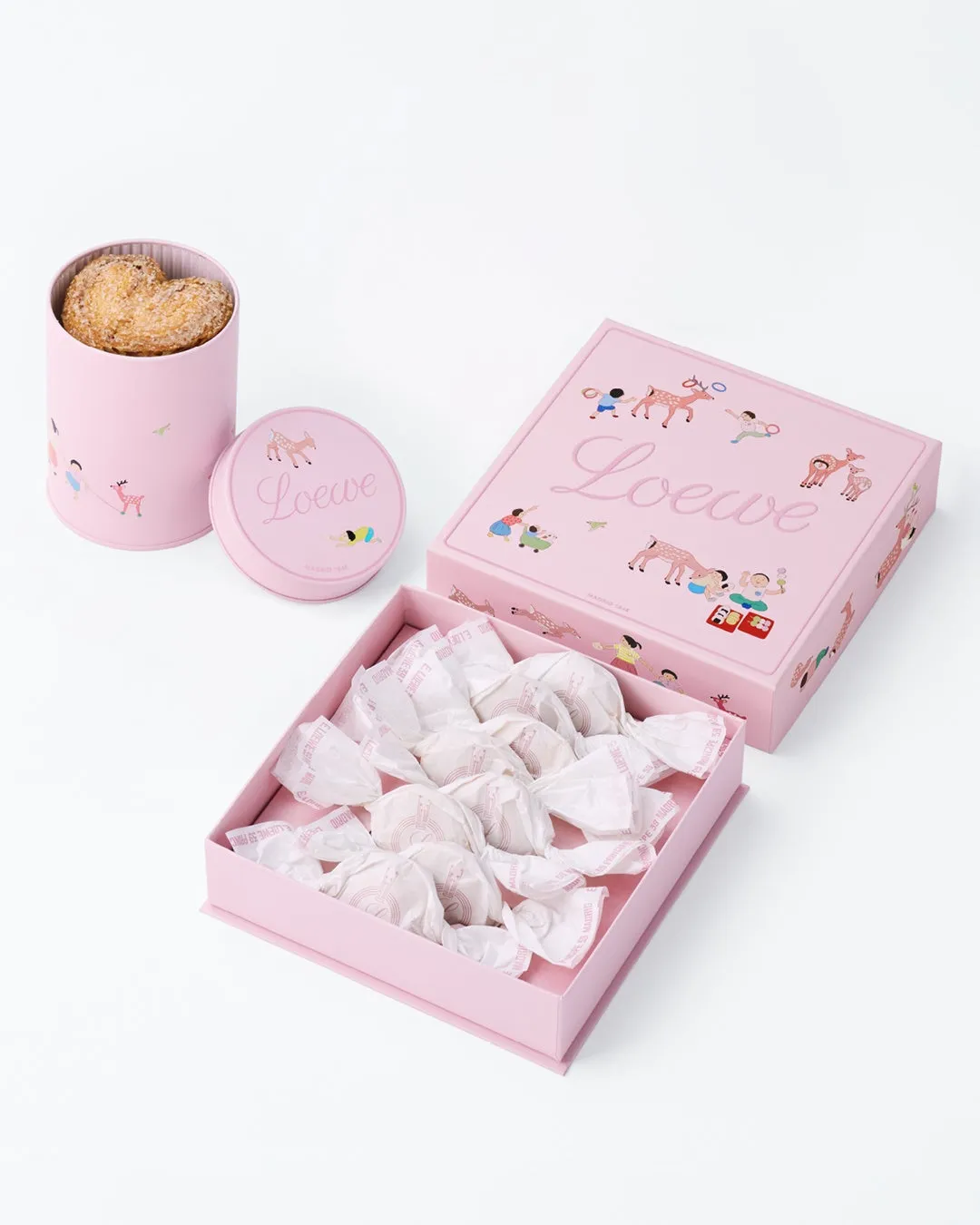 ピンク色のLoeweのギフトボックスとクッキーのセット。ボックスにはLoeweのロゴと子供たちのイラストが描かれています。クッキーは個別に包装されています。