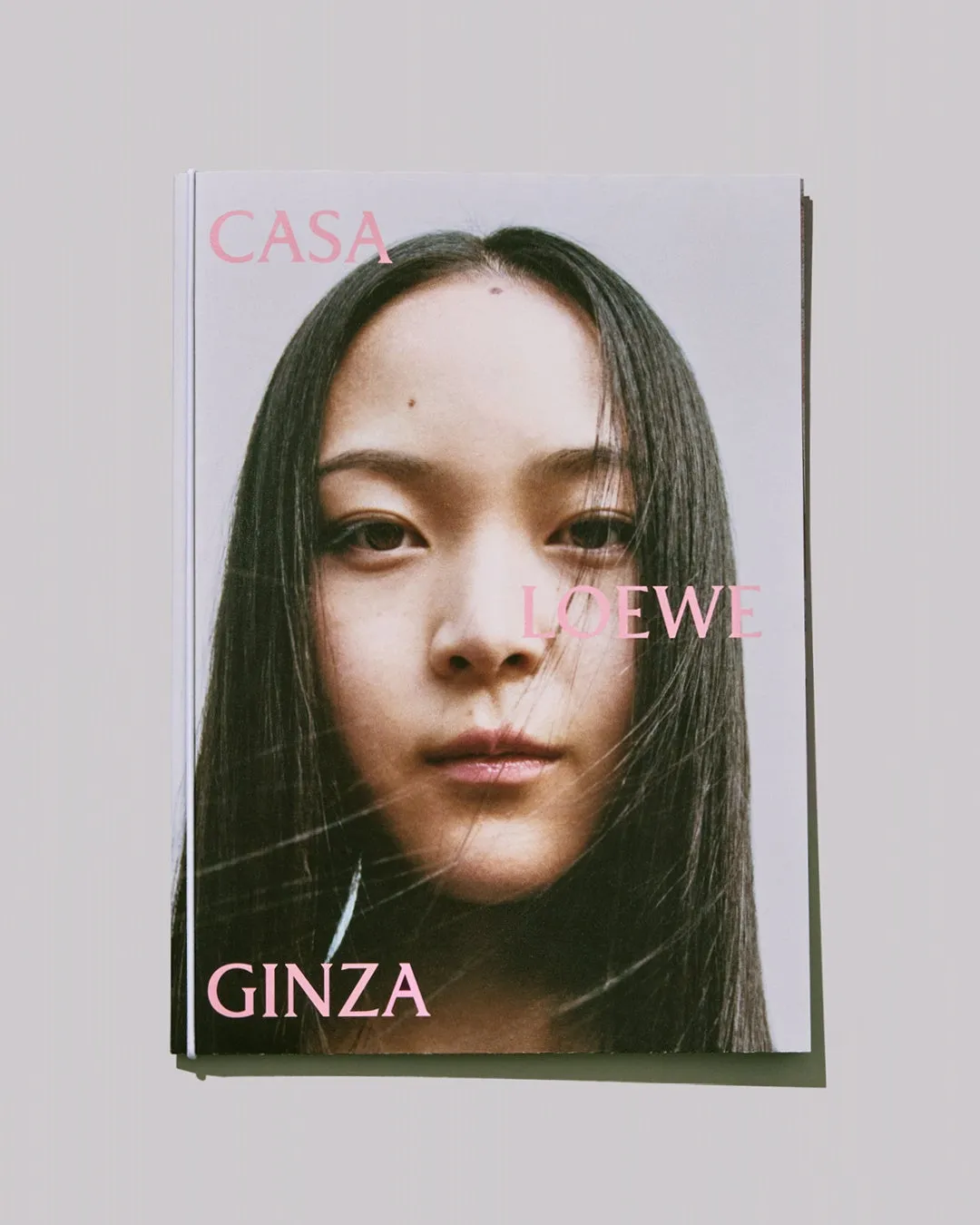 女性の顔が大きく写った雑誌の表紙。ピンク色の文字で「CASA LOEWE GINZA」と書かれている。