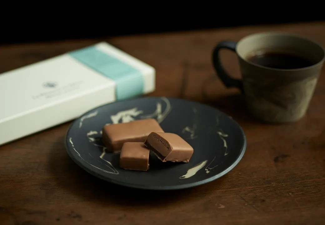 チョコレートとコーヒーが写った写真。チョコレートは皿に載っており、コーヒーはカップに入っている。背景にはチョコレートの箱が見える。