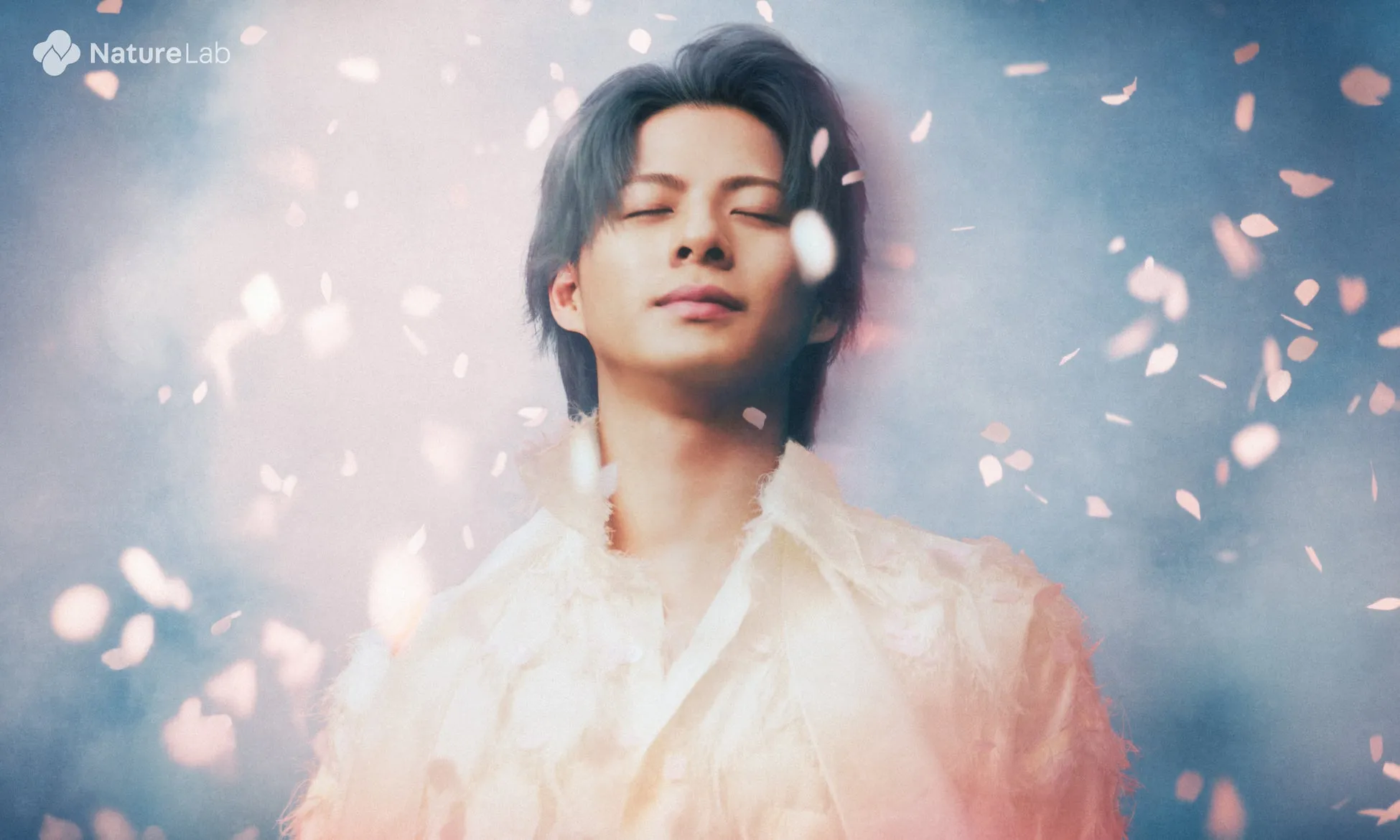 男性が目を閉じて微笑んでいるポートレート。背景には花びらが舞い、幻想的な雰囲気。