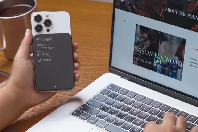 携帯電話に接続されたモバイルバッテリーと、ラップトップを使用している様子を示す画像です。
