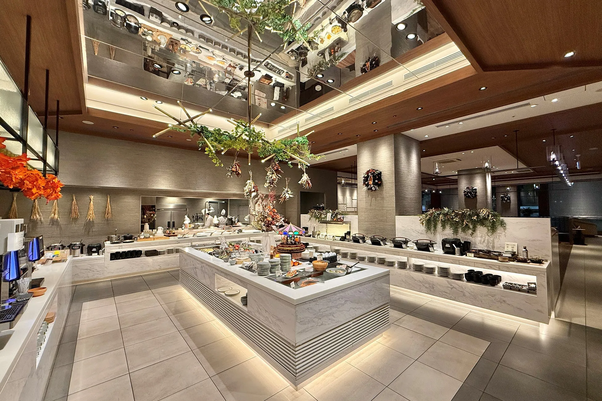ビュッフェスタイルのレストランのインテリア。中央に料理が並べられた大きなカウンターがあり、天井は鏡張りで、植物の装飾が施されています。