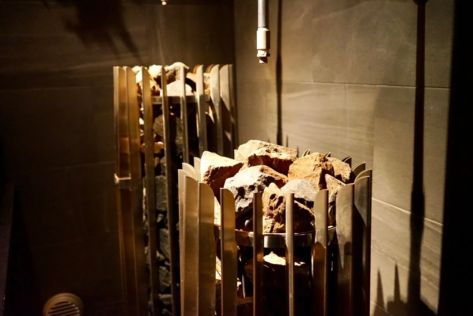 サウナストーブの写真。積み上げられた石が金属製のフレームに囲まれており、暗い背景に置かれている。