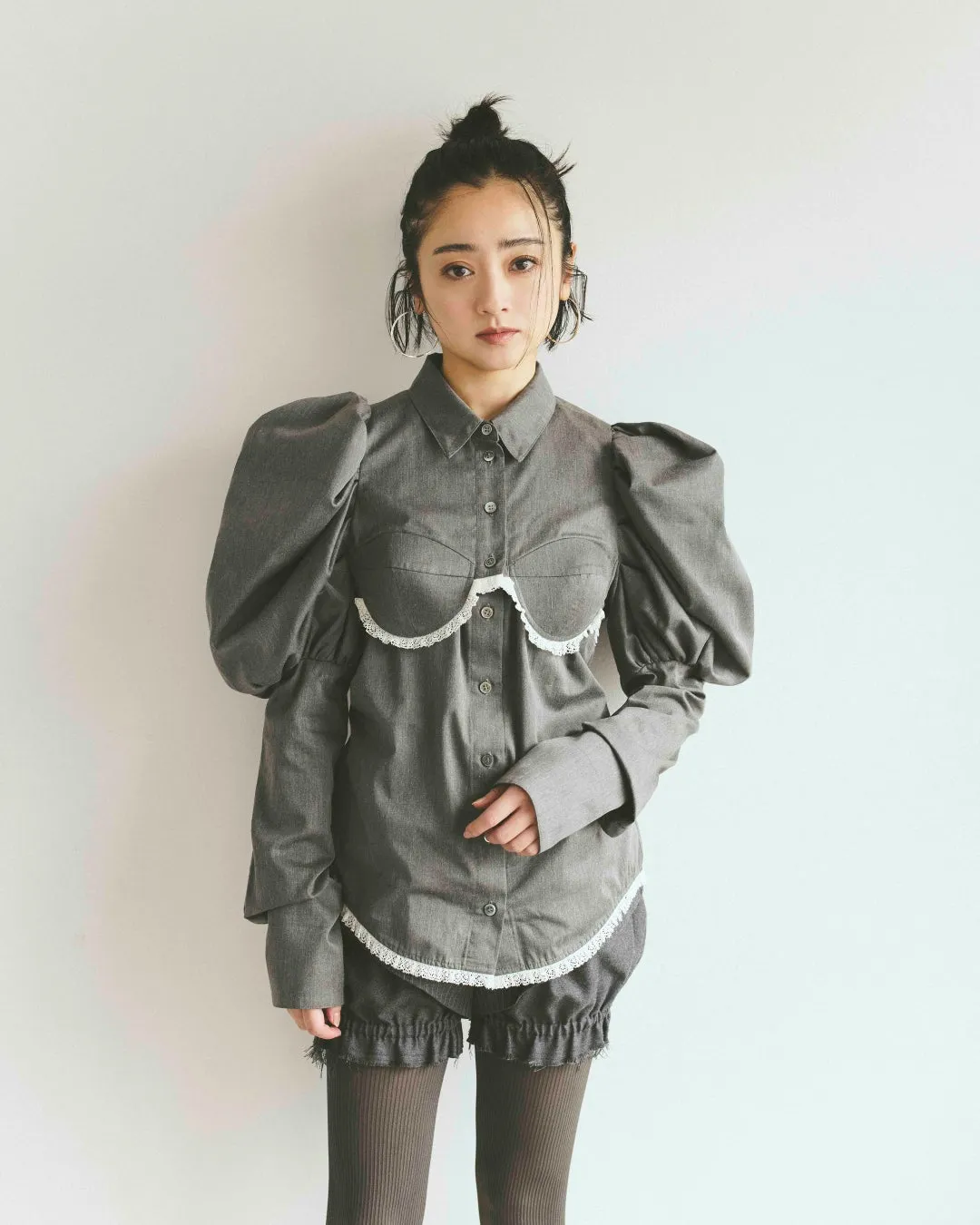 女性がグレーのシャツとショートパンツを着て立つスタイリング