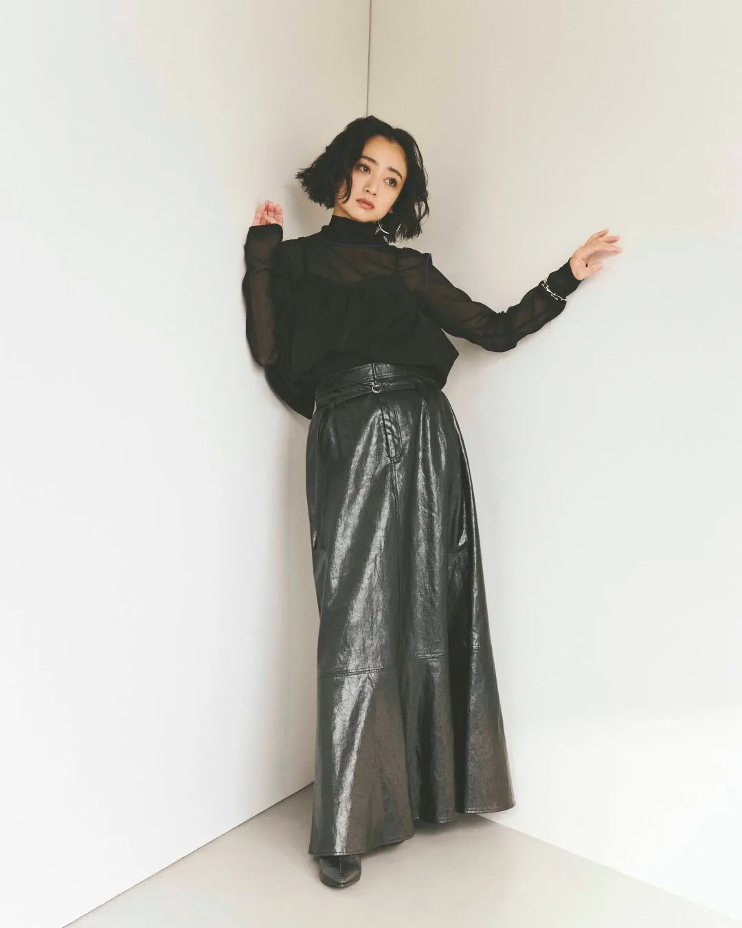 白い壁の角に寄りかかる女性のスタイリング