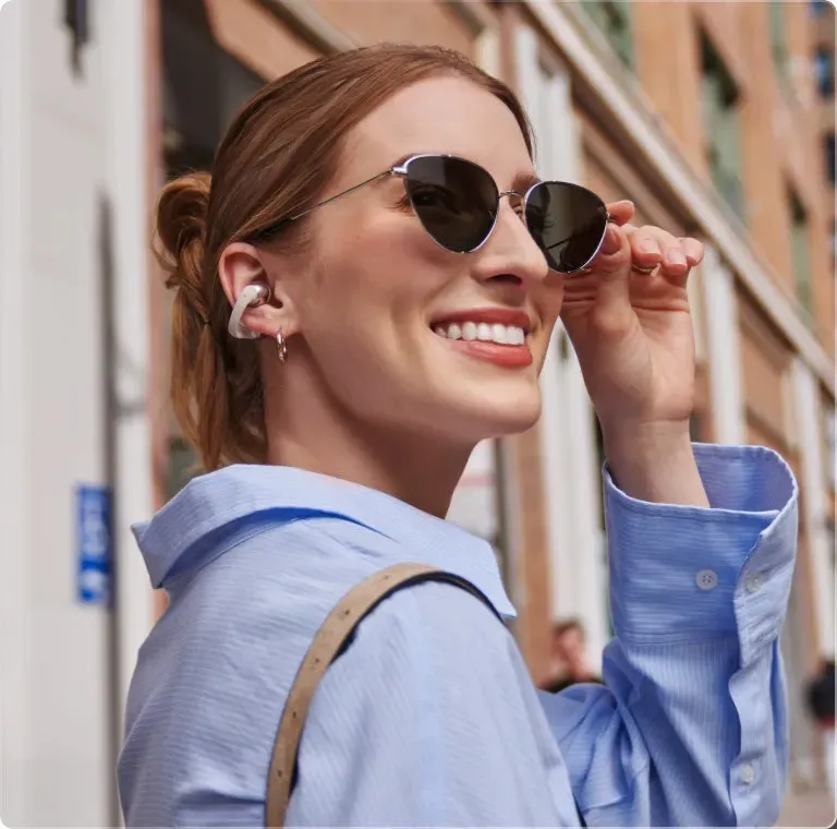 サングラスをかけた女性が笑顔で通りを歩いている様子。