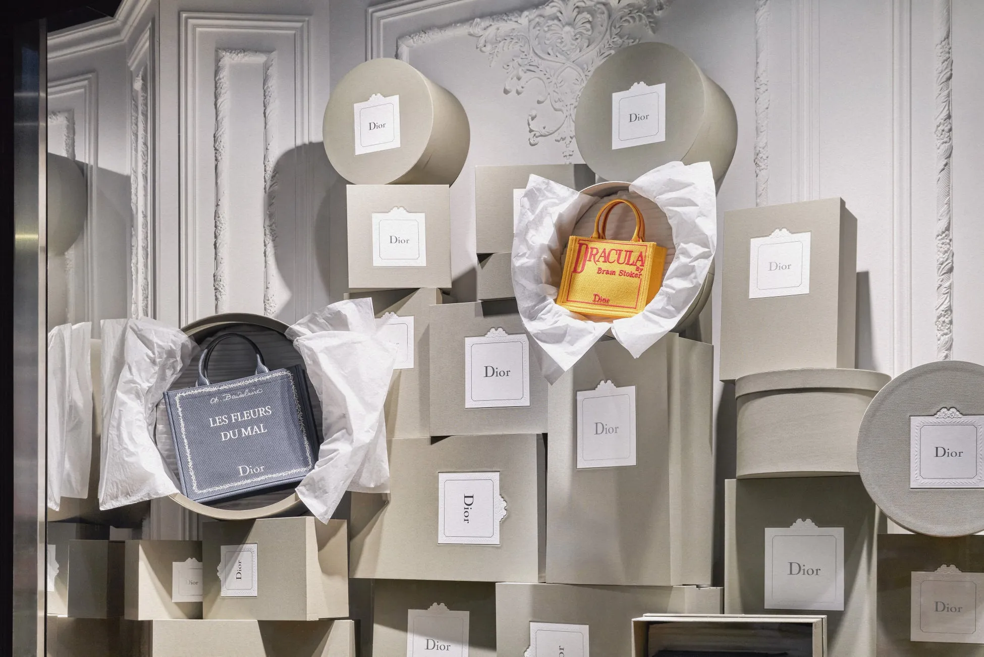ディオールのディスプレイ。 グレーの箱が積み重ねられており、その上にバッグが配置されている。バッグには「DRACULA」や「LES FLEURS DU MAL」の文字が記されている。箱には「Dior」のロゴが入ったラベルが貼られている。
