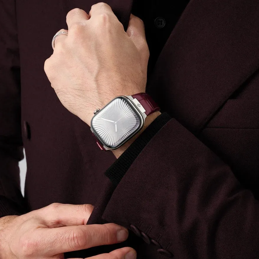 男性が腕時計を見せている様子。深紅色の革ベルトと、銀色の文字盤が特徴の洗練されたデザインの腕時計をしている。