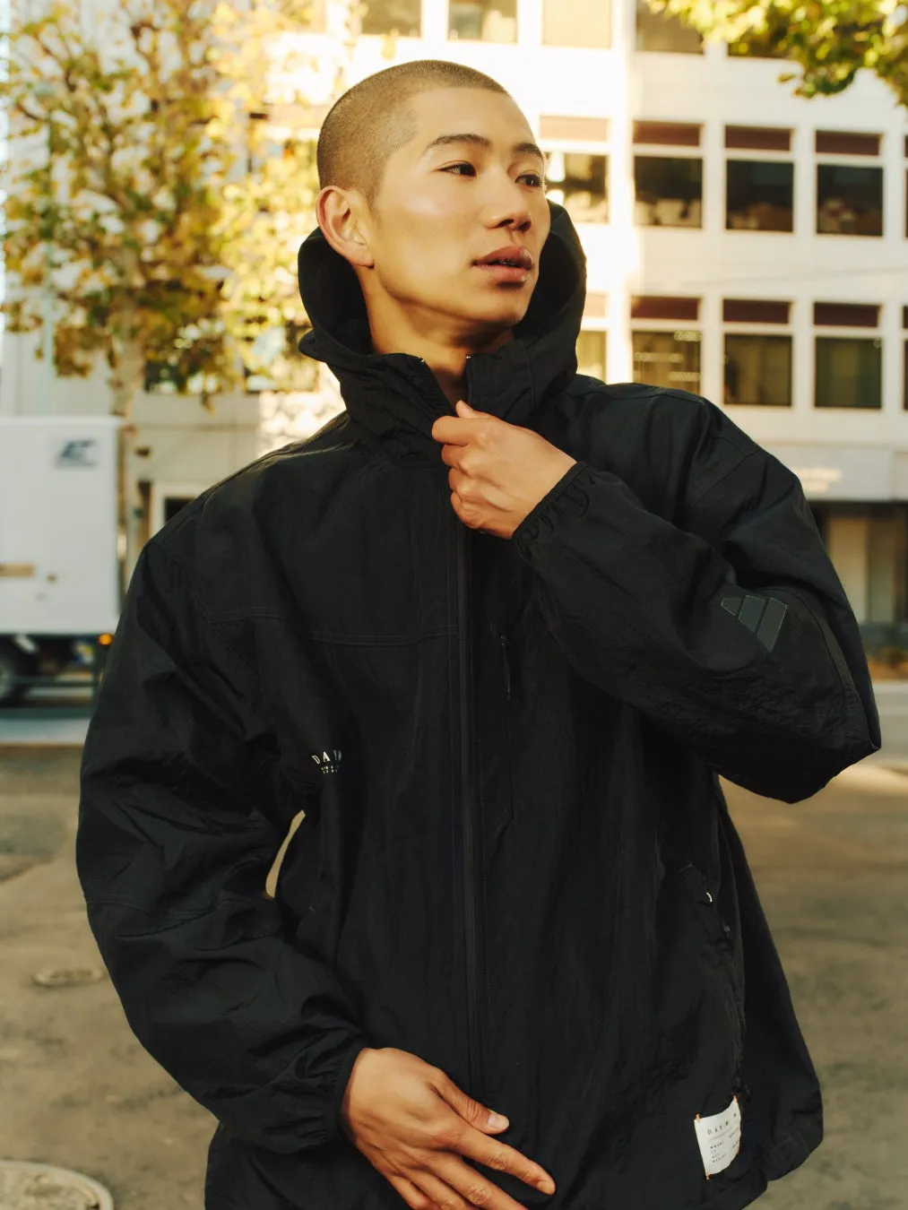 黒いジャケットを着た男性が屋外でポーズをとっています。彼は正面を向き、カメラから視線を外しています。