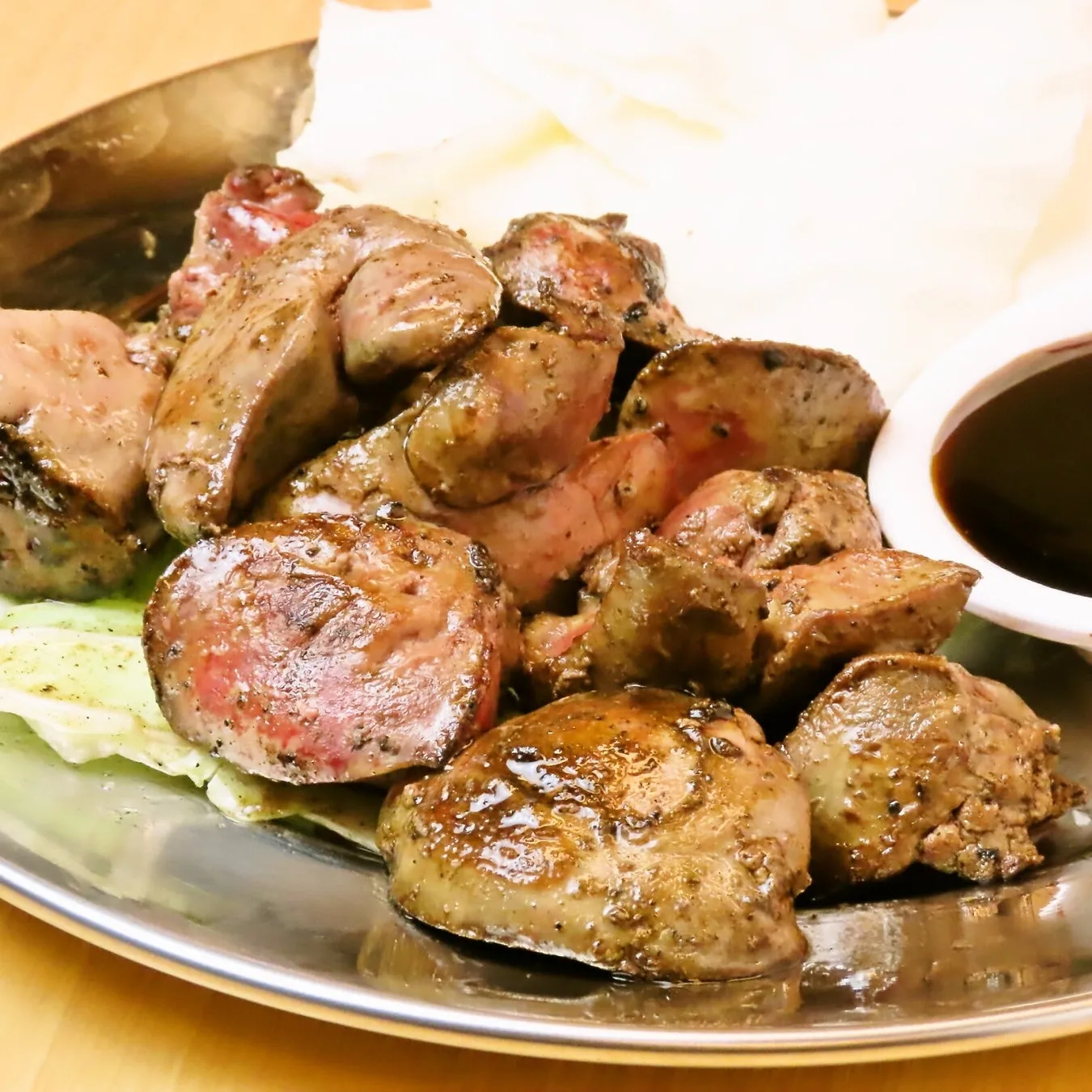 焼き鳥のレバーの盛り合わせ。お皿にレバーとキャベツ、ソースが添えられている。