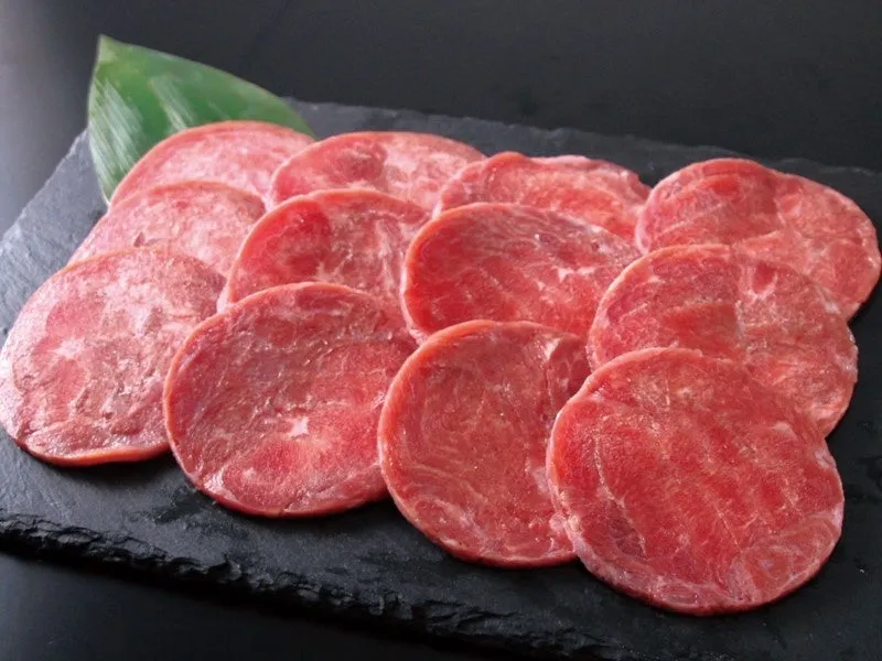 黒いお皿に並べられた、薄くスライスされた赤い肉のクローズアップ画像。