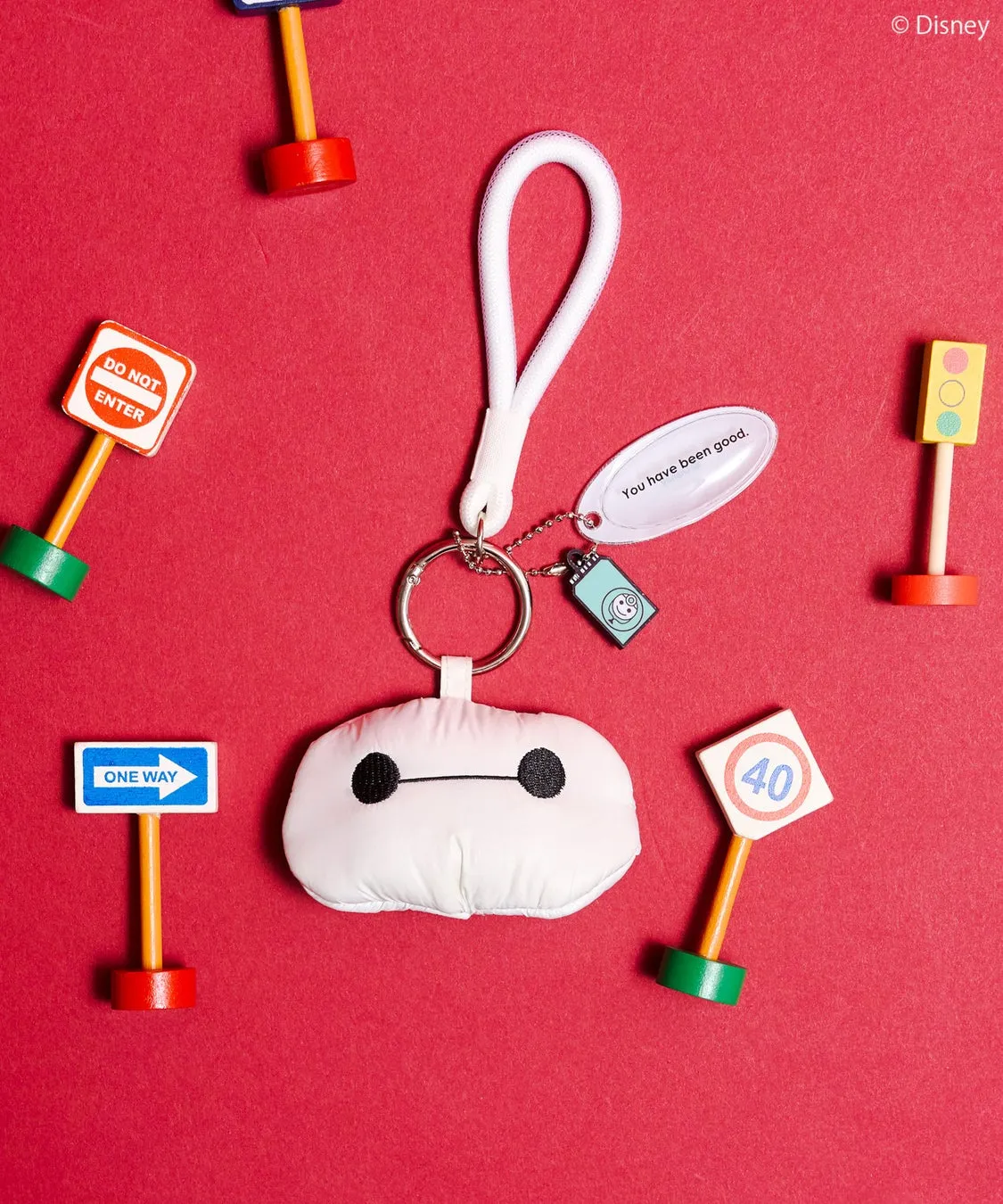 赤い背景に、ベイマックスのキーホルダーと、交通標識を模したおもちゃが配置された写真