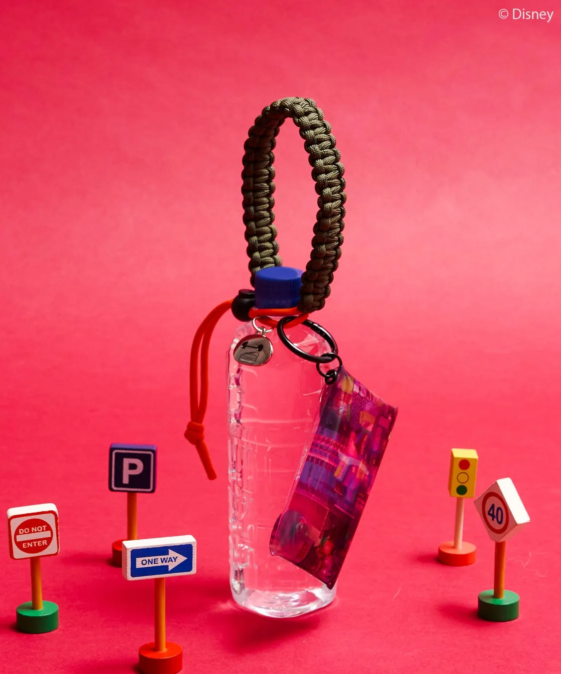 赤い背景に、水筒とキーホルダー、ミニチュアの標識が配置された写真