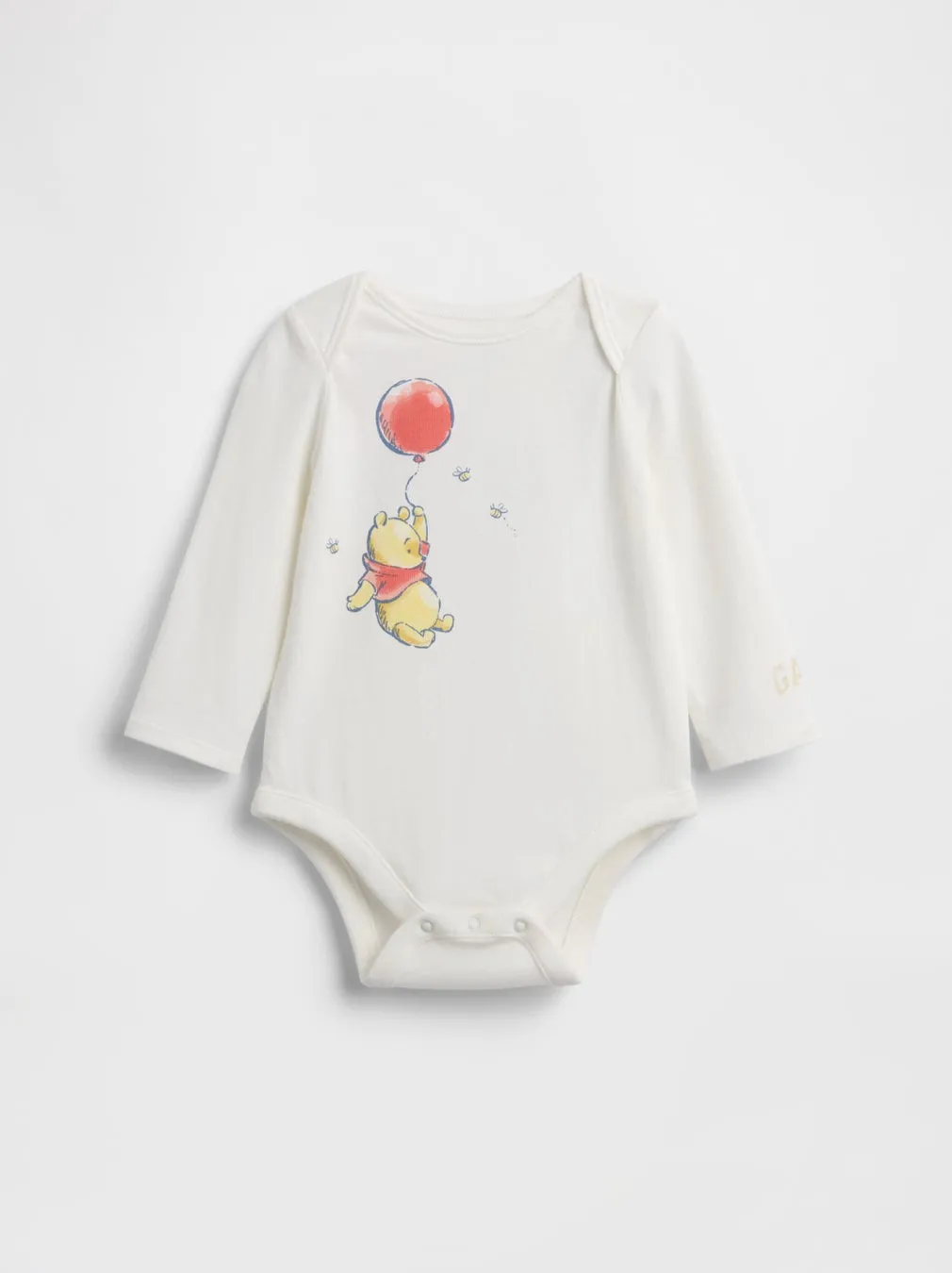 白地の長袖ベビーボディスーツ。中央には風船につかまるプーさんのイラストが描かれている。