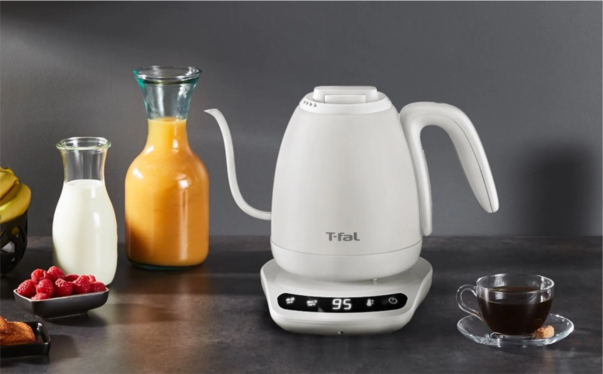 白い電気ケトル、ジュース、ミルク、コーヒー、ラズベリー、バナナのある朝食の場面。