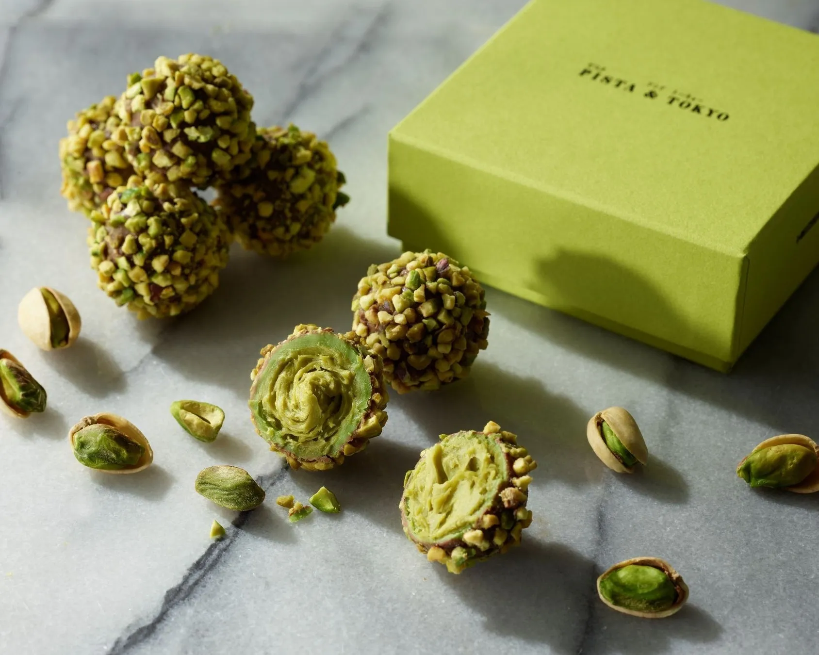 ピスタチオトリュフとピスタチオの画像。トリュフはピスタチオでコーティングされ、半分にカットされたものもある。箱には「PISTA & TOKYO」のロゴが入っている。