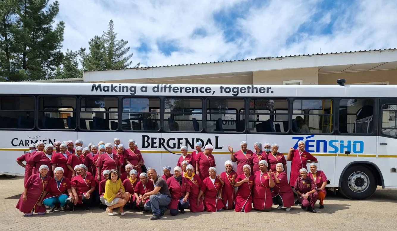 バスの前に集まってポーズをとる、帽子をかぶったグループの人々