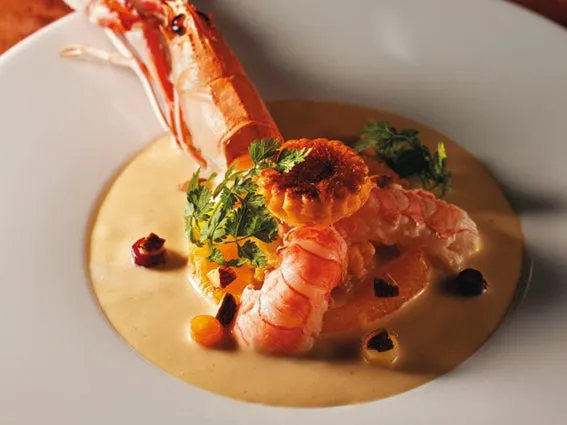 お皿に盛られた料理の写真。エビと小さなタルト、ソース、ハーブが添えられている。