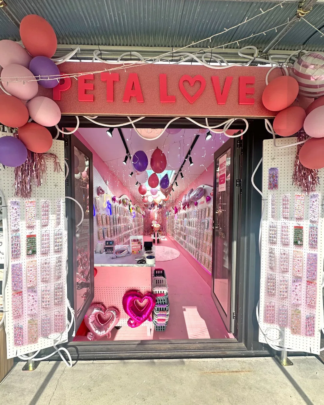 ピンク色の内装で、風船やアクセサリーが飾られたお店の入り口の写真です。「PETA LOVE」の文字が看板にあり、ハートの風船が飾られています。