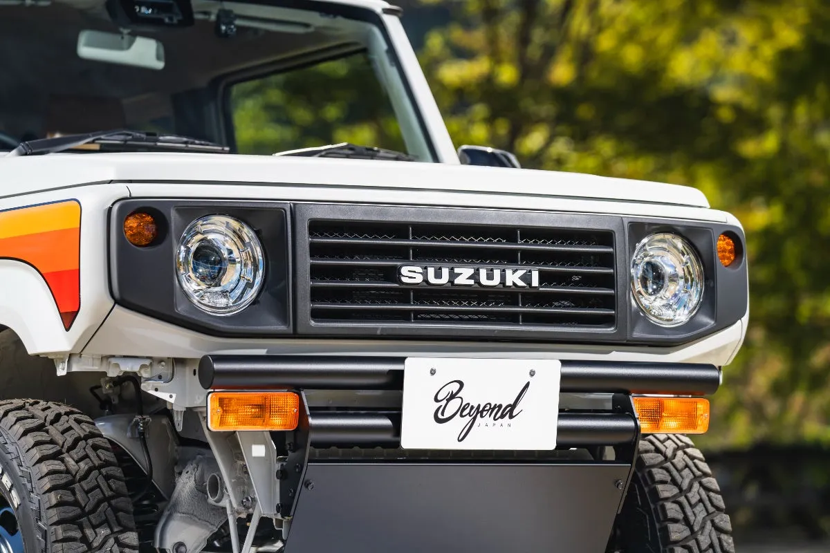 白いスズキジムニーのフロント部分。グリルには「SUZUKI」の文字、ナンバープレートには「Beyond JAPAN」の文字が記されている。