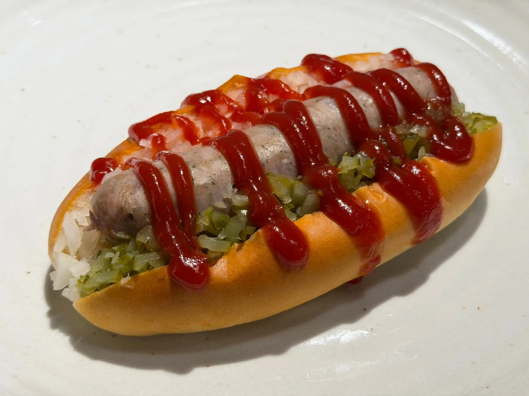 お皿に載ったホットドッグの写真です。ソーセージ、ピクルス、ケチャップがパンに挟まれています。