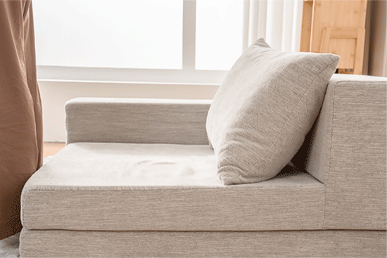 窓際に置かれたベージュのソファの写真です。クッションが一つ置かれています。