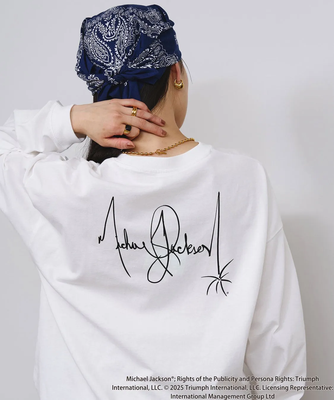 後ろ姿の女性が、マイケル・ジャクソンのサインがプリントされた白い長袖Tシャツを着ています。