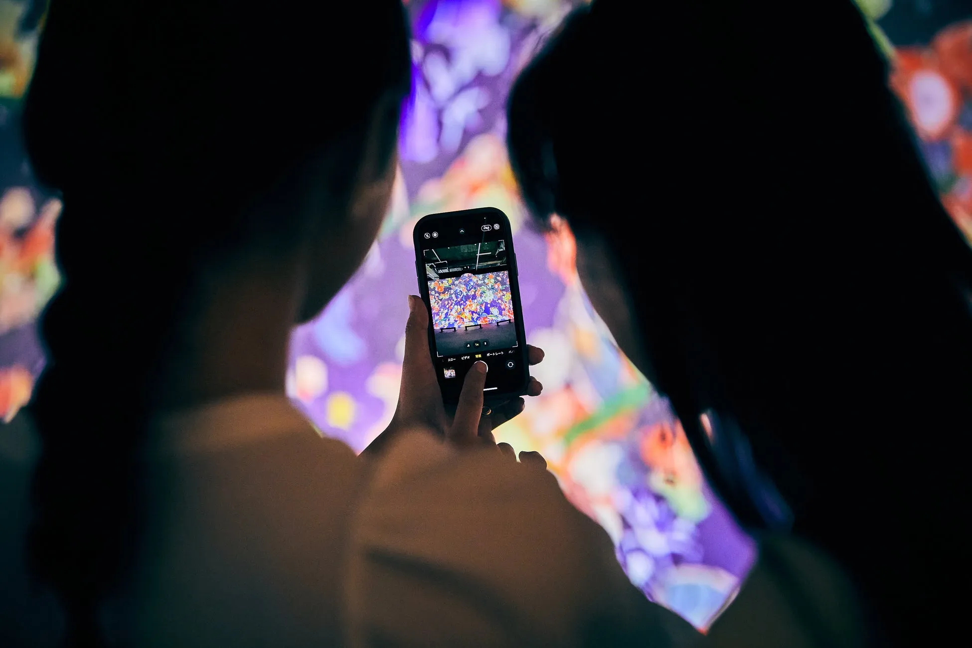 2人の人物が、スマートフォンでカラフルな芸術作品を撮影している様子を捉えた写真。