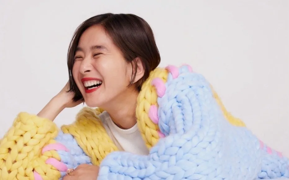 女性が笑顔で分厚いニットのセーターを着ている写真です。