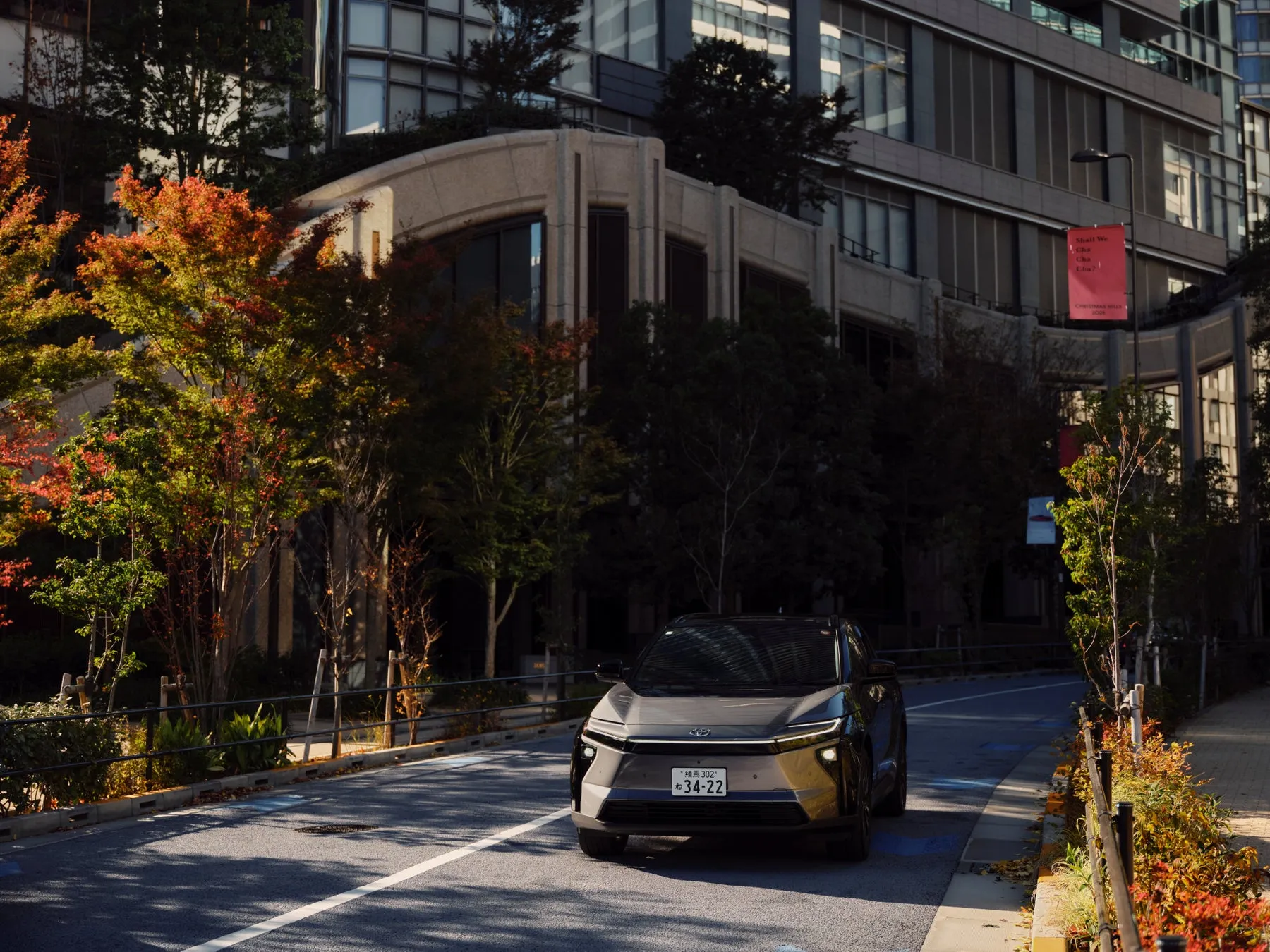 街路樹の紅葉と建物を背景に、トヨタbZ4Xが道路を走っている写真