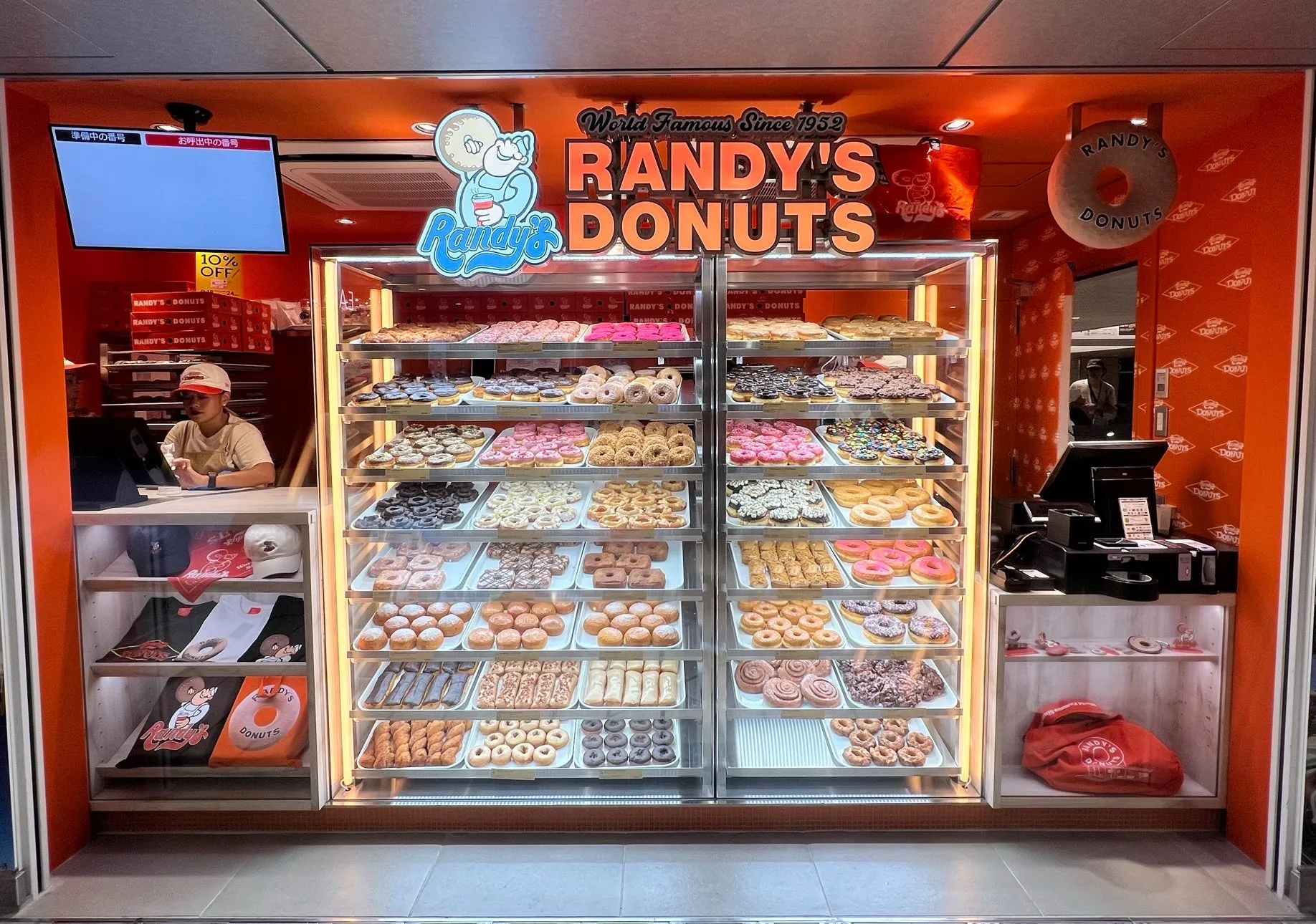Randy's Donutsの店舗の様子。ショーケースには様々な種類のドーナツが並び、店員が接客をしている。店内にはグッズも販売されている。