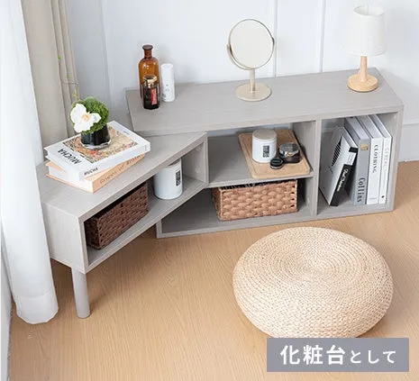 化粧台として使用されている、木製の収納棚と丸いクッションの画像です。棚の上には鏡、本、装飾品が置かれており、収納スペースも設けられています。全体的にシンプルで洗練された印象です。