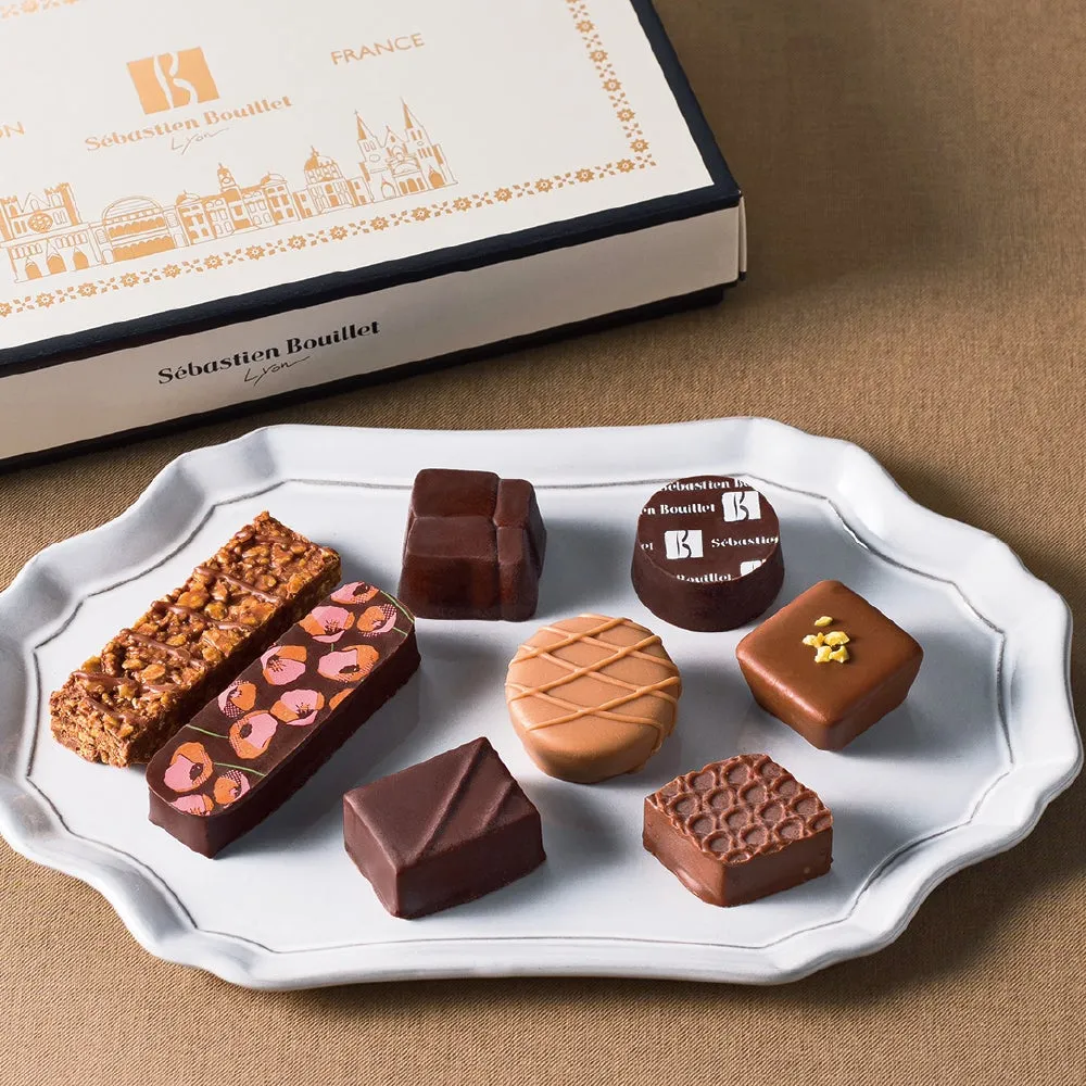セバスチャン・ブイエのチョコレートの詰め合わせ。様々な形のチョコレートが白いお皿に並べられており、上にはブランドロゴが印刷された箱が置かれている。