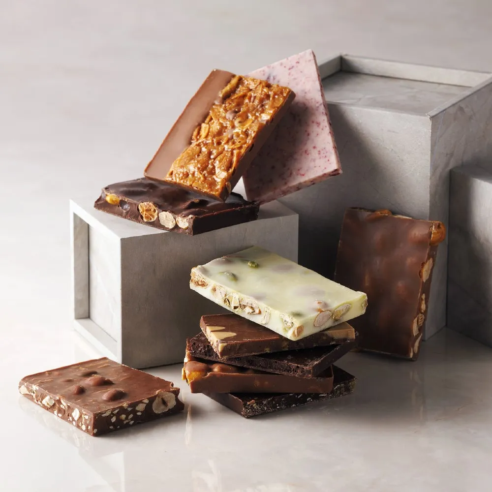 様々なチョコレートバーが積み重ねられた写真。ナッツやドライフルーツがトッピングされたものなど、様々なフレーバーとテクスチャのチョコレートが写っています。