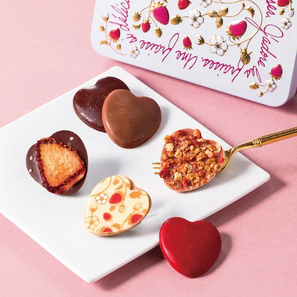 ハート型のチョコレートが並べられた写真。チョコレートは様々な種類があり、一部はドライストロベリーがトッピングされている。背景にはイチゴのイラストが描かれた缶が見える。