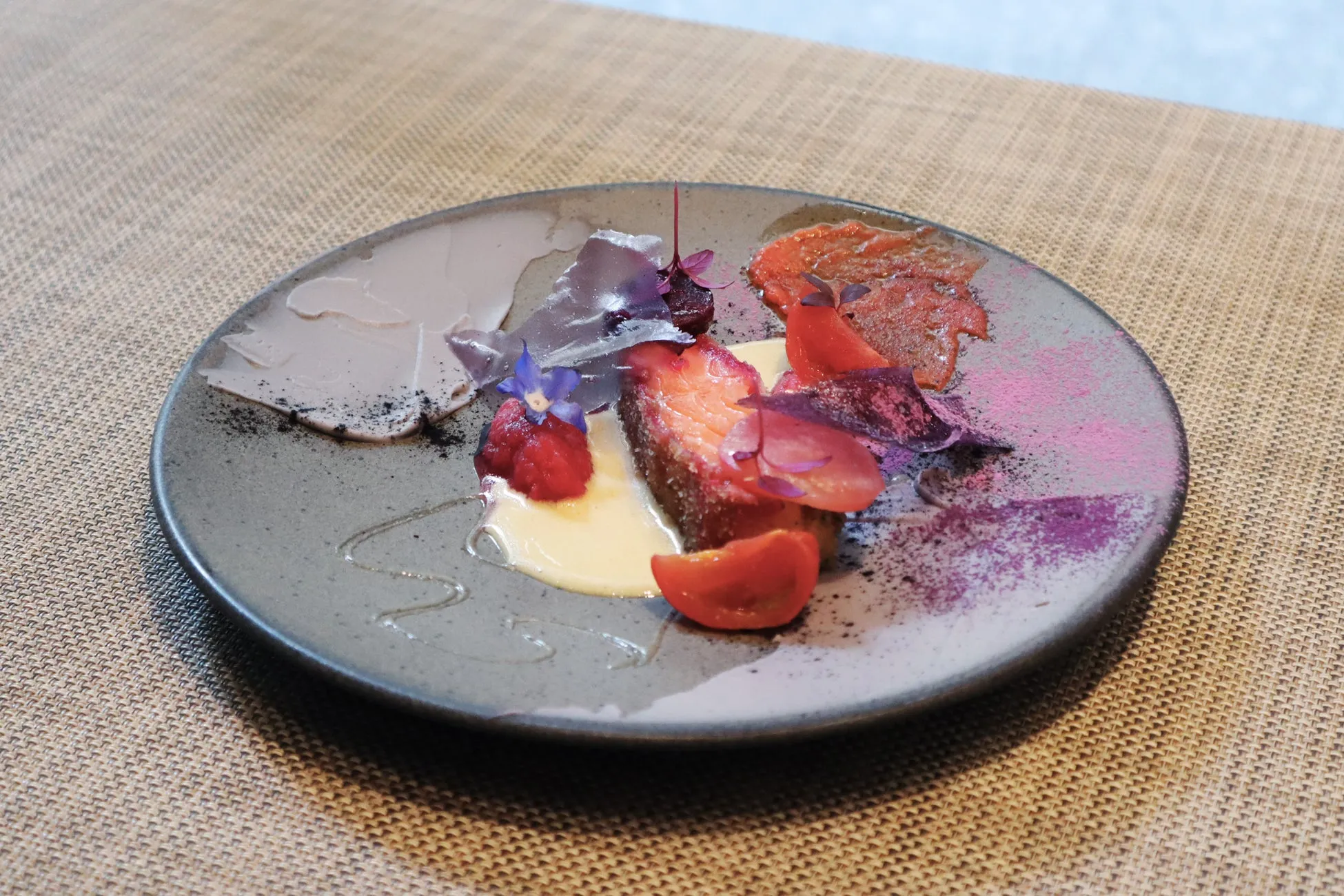 サーモン、トマト、紫色の野菜、花びらなどが美しく盛り付けられた料理