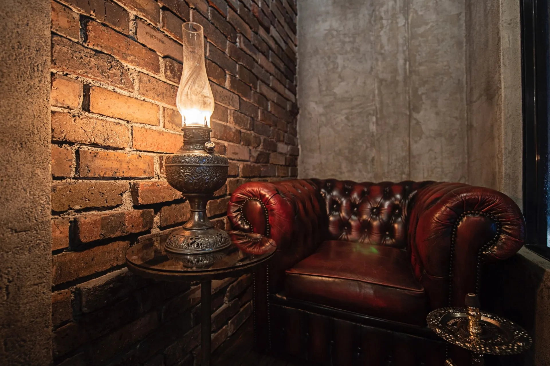レンガの壁と革張りの椅子がある部屋に置かれたアンティークランプの写真